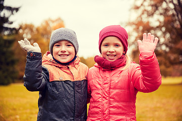 Image showing happy girl and boy waving hands in autumn park