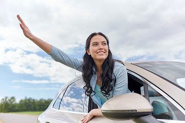 Image showing happy young woman driving in car and waving hand