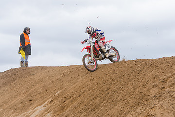 Image showing Volgograd, Russia - April 19, 2015: Motorcycle racer moves over the hill, a volunteer was looking at him, at the stage of the Open Championship Motorcycle Cross Country Cup Volgograd Region Governor