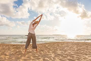 Image showing Woman practicing yoga on sea beach at sunset.