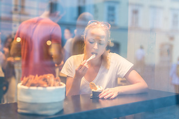 Image showing Young pretty woman eating icecream in gelateria.