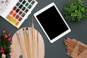 Image showing The workspace of artist with laptop, paints, paintbrushes, flowers on black