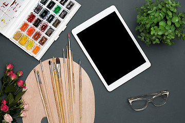 Image showing The workspace of artist with laptop, paints, paintbrushes, flowers on black