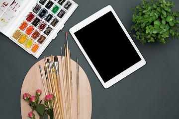 Image showing The workspace of artist with laptop, paints, paintbrushes, flowers on black