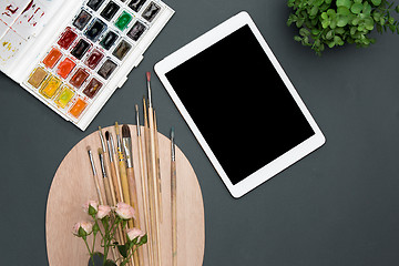 Image showing The workspace of artist with laptop, paints, paintbrushes, flowers on black