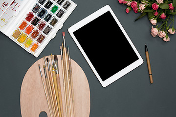 Image showing The workspace of artist with laptop, paints, paintbrushes, flowers on black