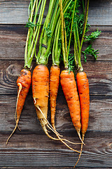 Image showing Raw carrot with green leaves on wooden background