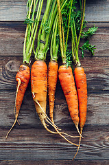 Image showing Raw carrot with green leaves on wooden background