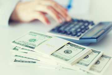 Image showing close up of hand counting money with calculator