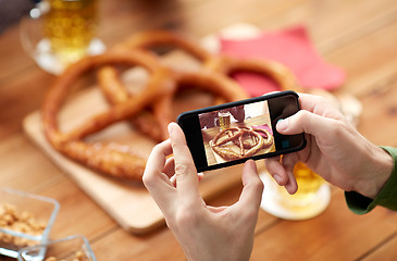 Image showing close up of hands picturing pretzel by smartphone