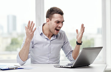 Image showing angry businessman with laptop and papers in office