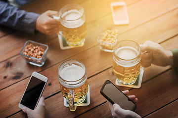 Image showing close up of hands with smartphones and beer at bar