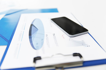 Image showing close up of smartphone and clipboard with charts