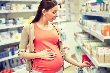 Image showing happy pregnant woman choosing medicine at pharmacy