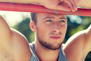 Image showing young man exercising on horizontal bar outdoors