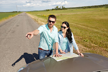 Image showing happy man and woman with road map on car hood