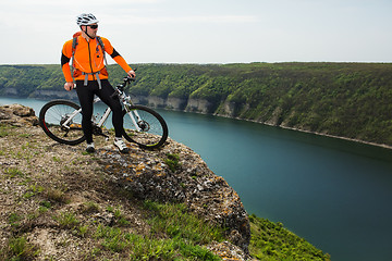 Image showing Cyclist in Orange Wear Riding the Bike above River