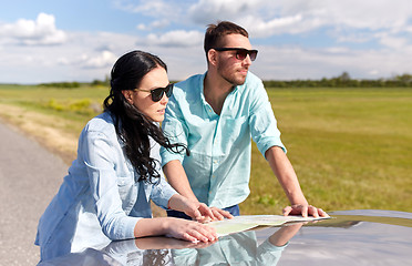 Image showing happy man and woman with road map on car hood