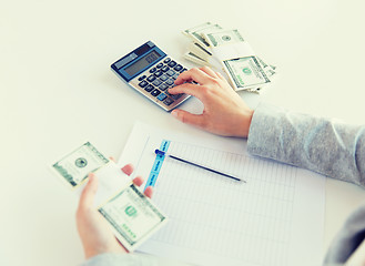 Image showing close up of hands counting money with calculator