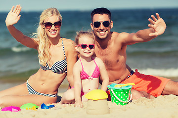 Image showing happy family with sand toys waving hands on beach