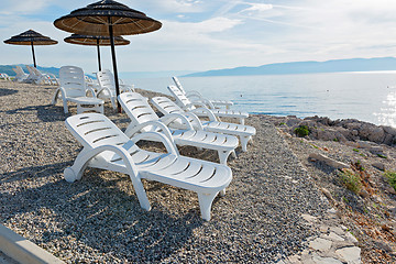 Image showing Pebble beach with chaise-longues and umbrellas