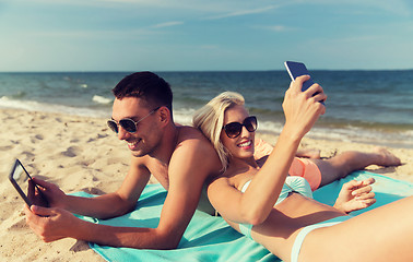 Image showing happy couple with modern gadgets lying on beach