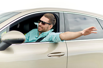 Image showing happy man in shades driving car and waving hand