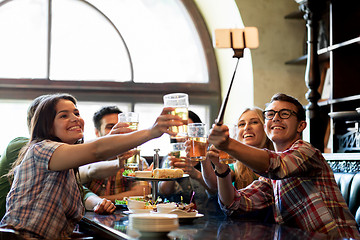 Image showing happy friends with selfie stick at bar or pub