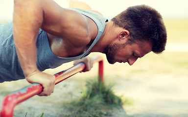 Image showing young man exercising on horizontal bar outdoors