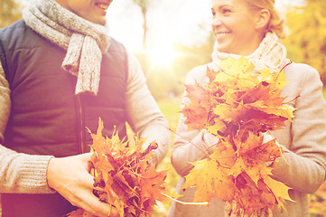Image showing smiling couple with maple leaves in autumn park
