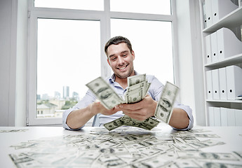 Image showing happy businessman with heap of money in office