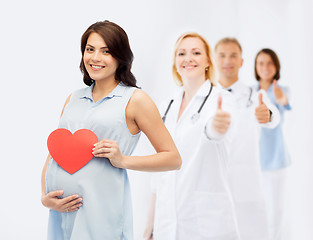 Image showing happy pregnant woman with red heart touching belly