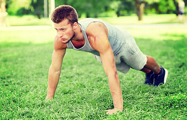 Image showing young man doing push ups on grass in summer park