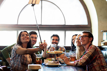 Image showing happy friends with selfie stick at bar or pub