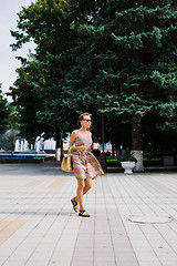 Image showing Young brunette woman with coffee cup walking in city