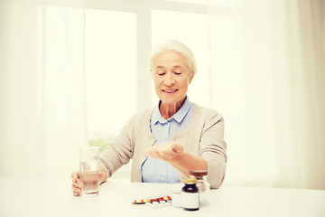 Image showing happy senior woman with water and medicine at home