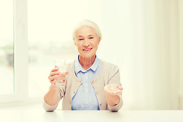 Image showing happy senior woman with water and medicine at home