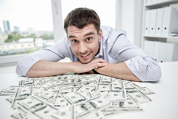 Image showing happy businessman with heap of money in office