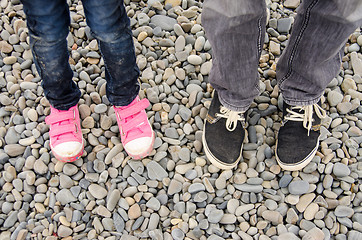 Image showing Two pairs of feet in sneakers, adults and children, are on the pebble