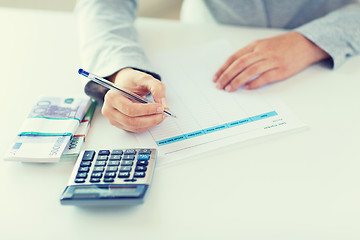 Image showing close up of hands counting money with calculator