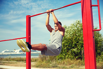 Image showing young man exercising on horizontal bar outdoors