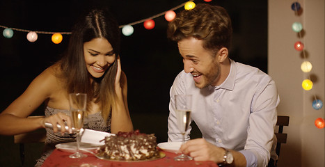 Image showing Elated young couple joking as they cut the cake