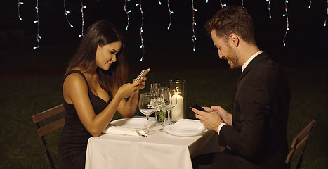 Image showing Young couple checking their mobiles during dinner
