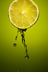 Image showing Lime slice and splash of juice isolated on green background.