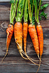 Image showing Raw carrot with green leaves on wooden background