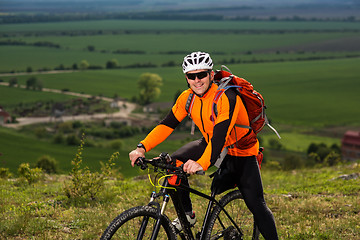 Image showing Young man cycling on a rural road through green meadow