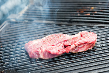 Image showing raw steak with spices on metal grill