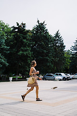 Image showing Young brunette woman with coffee cup walking in city