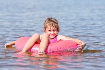 Image showing Five-year girl swims in the river sat on the lap swimming and happily looks into the frame