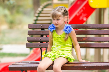 Image showing Portrait of upset five year old girl who is sitting on the bench on the background of the playground